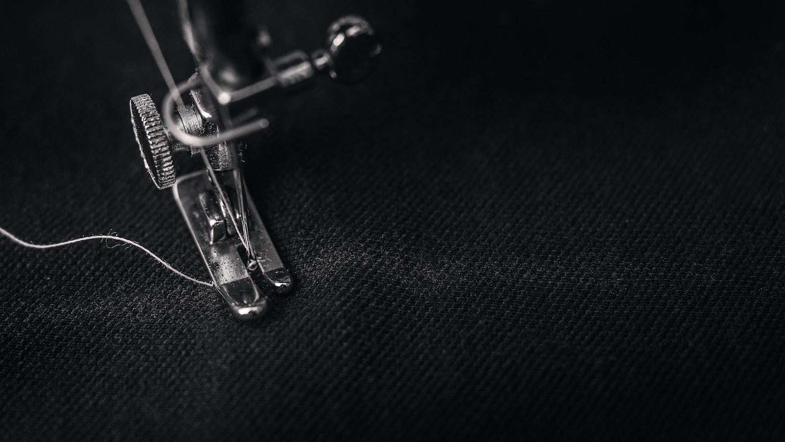 Black-and-white close-up of a sewing machine foot stitching dark fabric