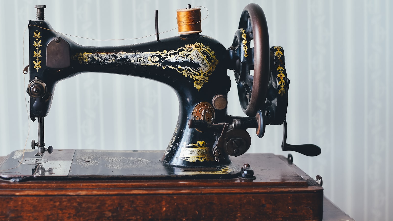 A vintage black sewing machine with gold floral decals rests on a wooden base