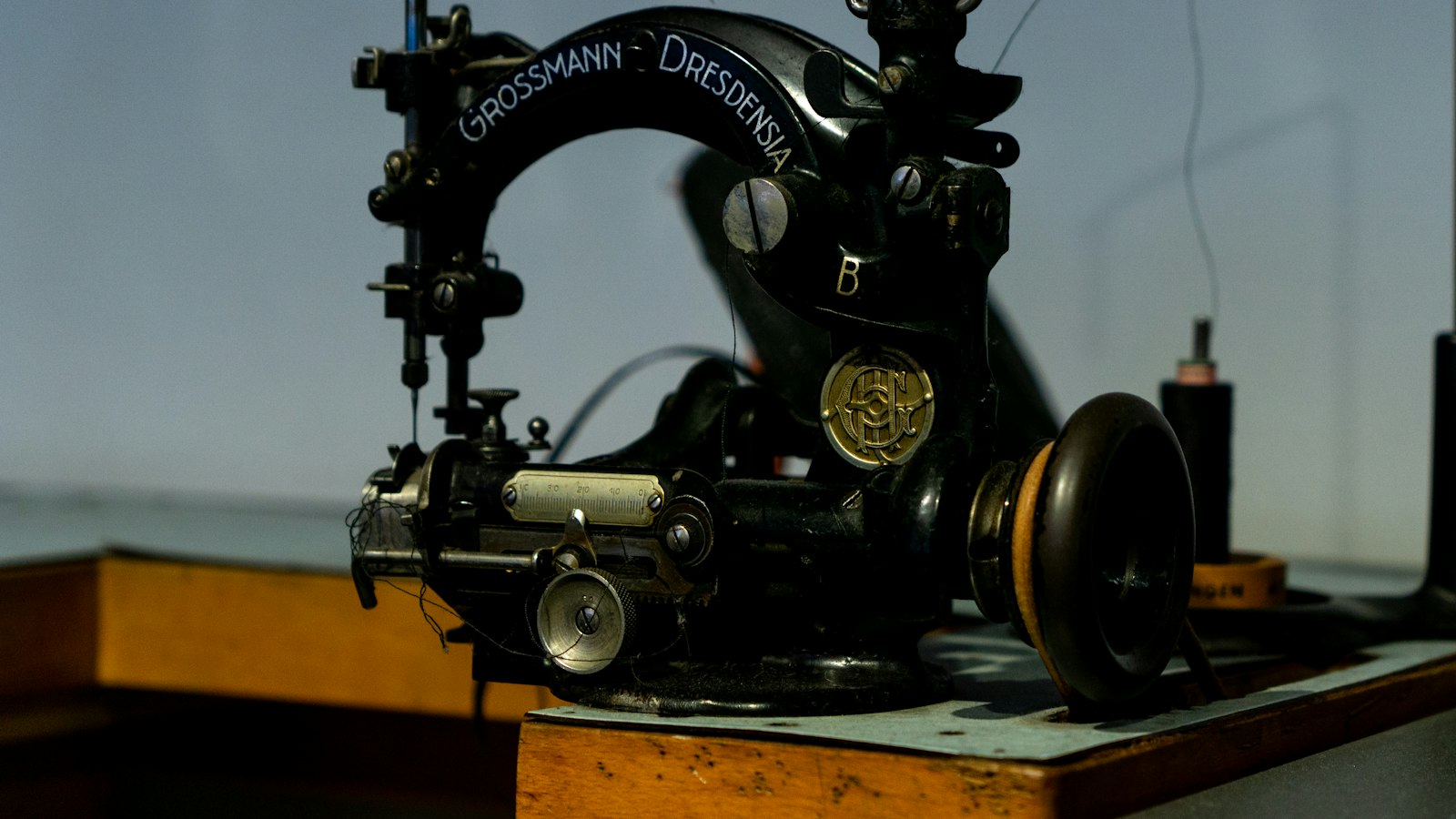 An antique black sewing machine rests on a wooden table, inscribed with "GROSSMANN DRESDENSIA