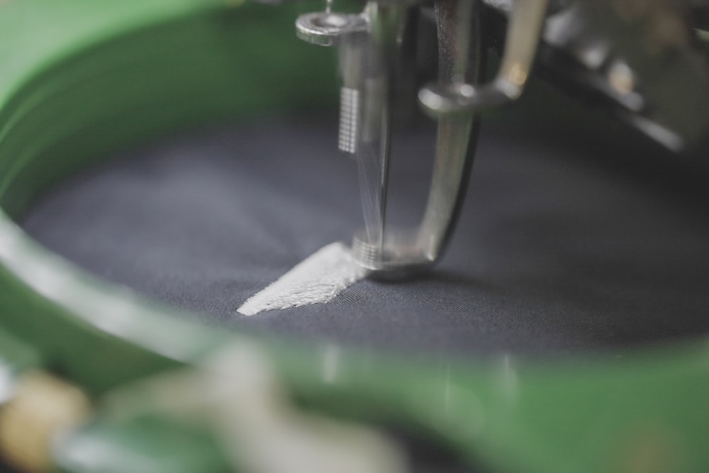 Close-up of a sewing machine needle stitching white thread onto dark fabric in a green hoop